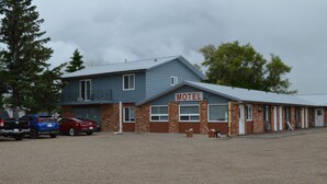 Un motel avec une façade en briques de deux étages, un panneau indicateur et un parking en gravier où sont garées plusieurs voitures.