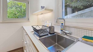 A kitchen with a stainless steel sink, a window with a view of greenery, and a white tiled backsplash. - Studio with terrace for 2 people (Baška)