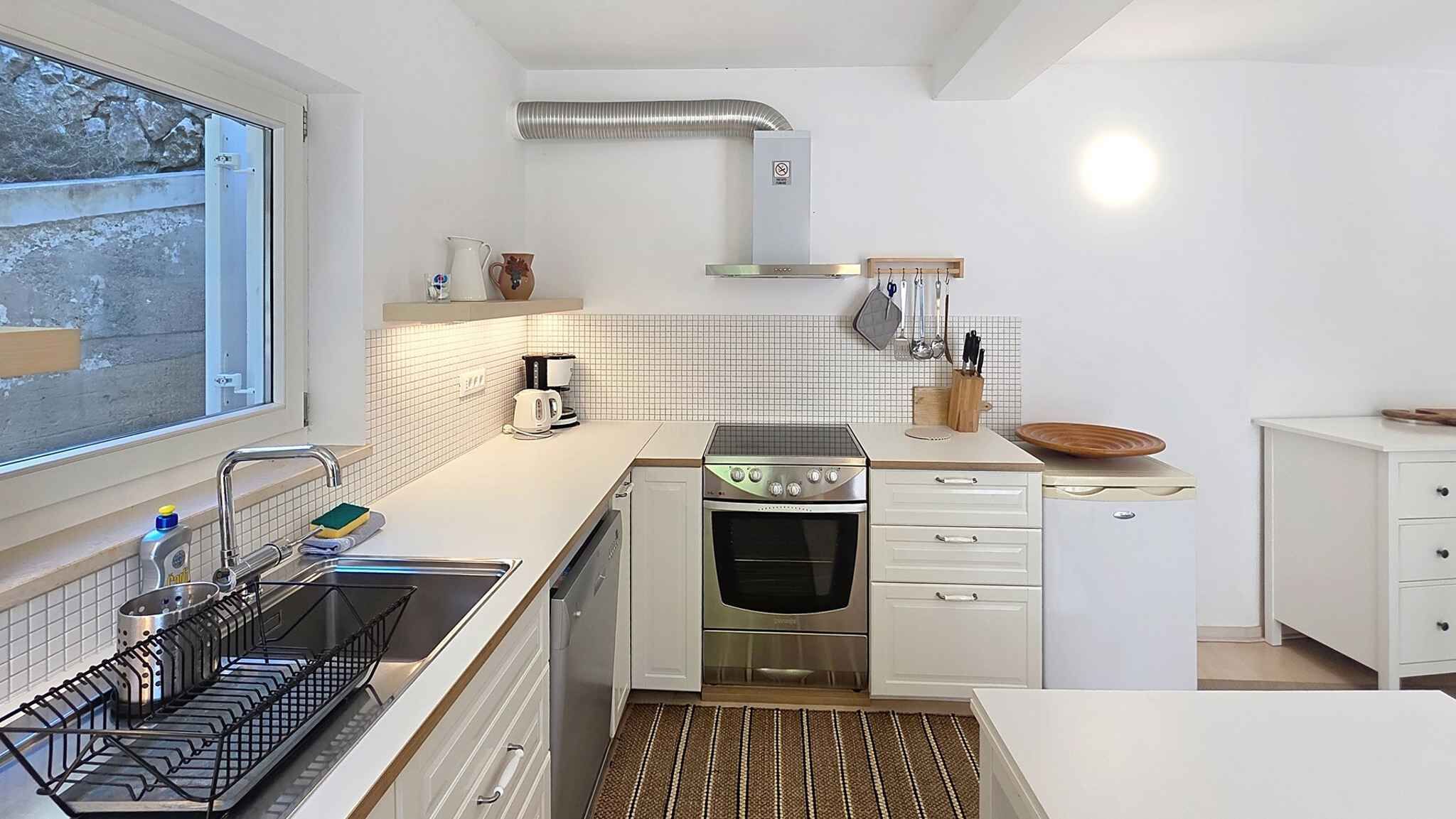 A compact kitchen with a sink, stove, and oven, a window with a view, and a tiled backsplash.