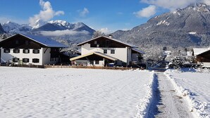 Un village enneigé, avec des bâtiments de style chalet traditionnel, un ciel dégagé et des montagnes enneigées en arrière-plan.