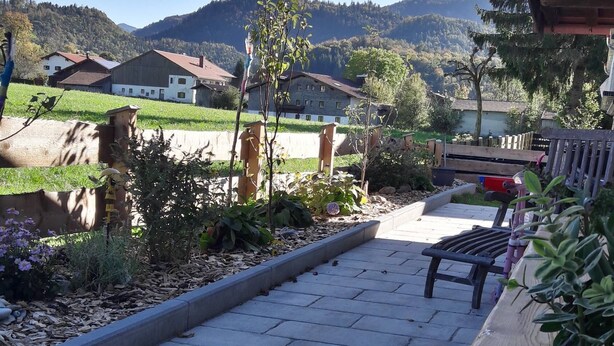Un chemin pavé mène à un banc, qui est entouré d’un jardin agrémenté de plantes et d’une clôture en bois.