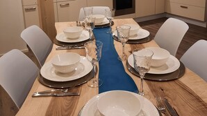 Une cuisine moderne avec des meubles blancs, un plan de travail bleu et un coin repas agrémenté d’assiettes et de verres blancs.
