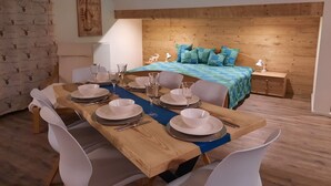 Un coin repas avec une table en bois dressée pour quatre personnes, un lit avec une couverture bleue et une tête de lit en bois.