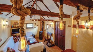 Un'accogliente stanza con un divano, un tavolo in legno e una sedia. Sono presenti luci a sospensione e un soffitto in legno.