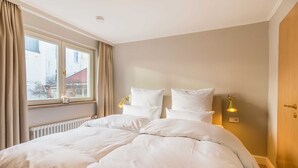 Une chambre à coucher avec un grand lit, deux lampes de chevet, une fenêtre avec des rideaux et un radiateur.