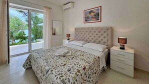 Quarto com cama, mesa de cabeceira, estante com gavetas, janela com cortinas e um quadro na parede.