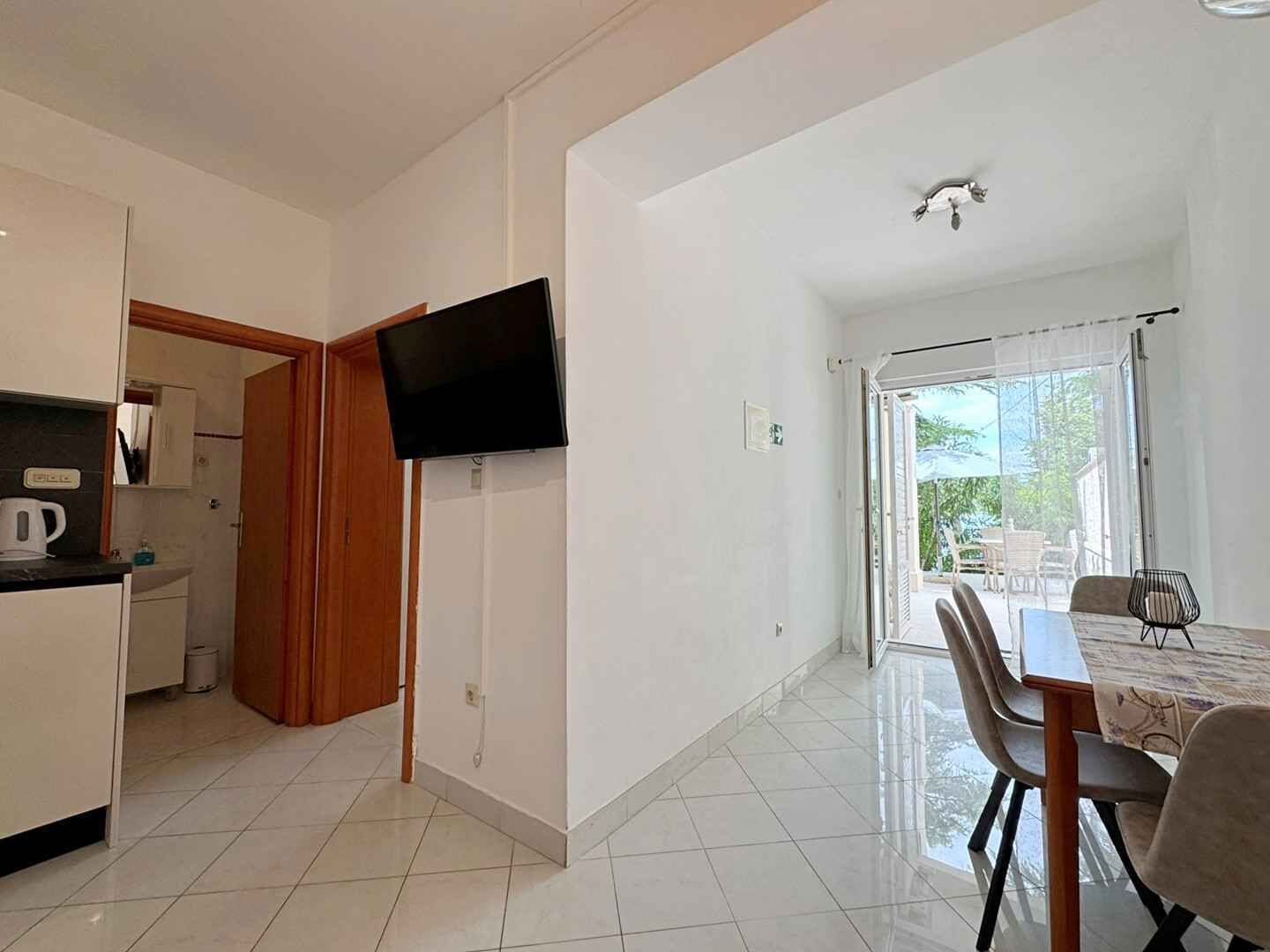A modern kitchen with a flat-screen TV, a dining area with a table and chairs, and a balcony with a view.