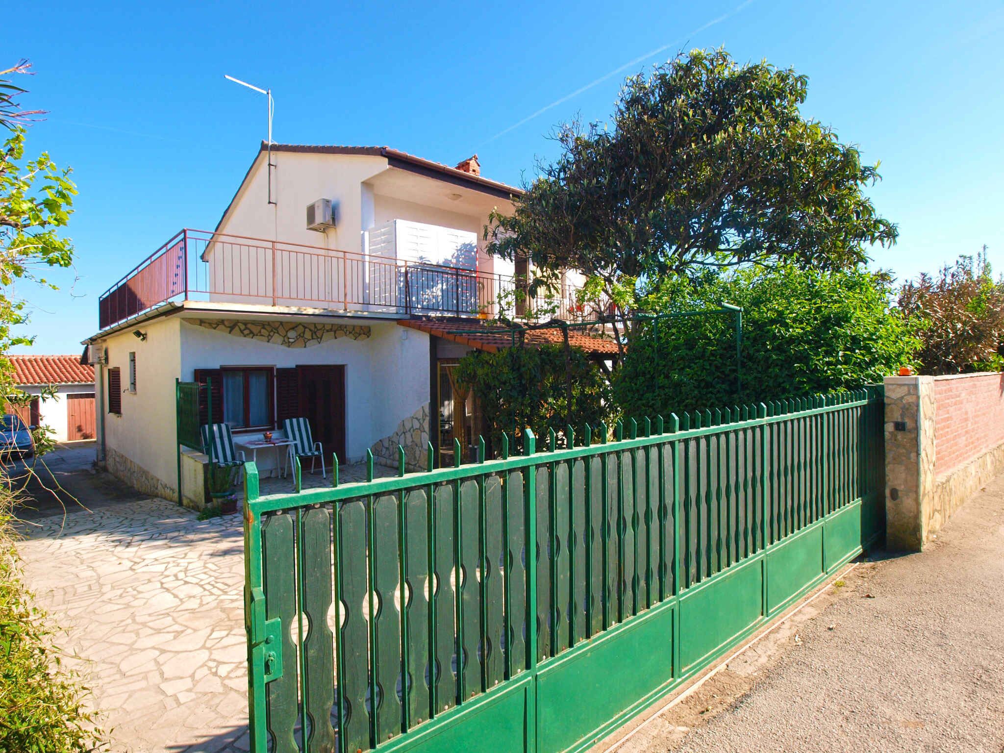 A two-story house with a balcony, a stone facade, and a green metal fence.