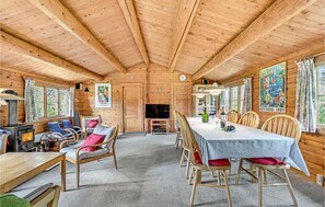 A wooden cabin interior with a dining area, a television, and a wood stove.