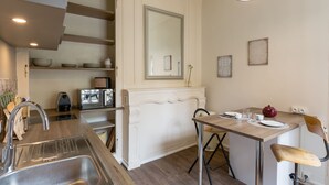 A compact kitchen with a sink, a dining table with chairs, a mirror, and a small countertop with a kettle and cups. - AMBRE - Studio de charme en plein coeur du centre historique (Rennes)