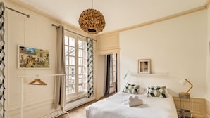 A bedroom with a large bed, a hanging light fixture, a radiator, and a window with curtains. - AMBRE - Studio de charme en plein coeur du centre historique (Rennes)