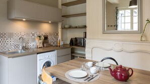 A kitchen with a washing machine, sink, and a dining table set with a red teapot, cups, and plates. - AMBRE - Studio de charme en plein coeur du centre historique (Rennes)