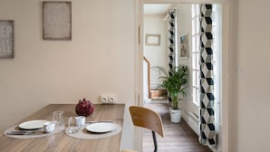 A dining area with a wooden table set for four, a red teapot, and two framed pictures on the wall. - AMBRE - Studio de charme en plein coeur du centre historique (Rennes)