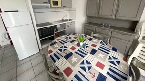 Eine kompakte Küche mit Esstisch, weißen Schränken, einer Mikrowelle und einem Kühlschrank.