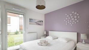 A bedroom with a bed, a nightstand, a lamp, a picture on the wall, and a view through the door. - LE GARDEN - Vaste appartement avec Jardin et terrasse (Dinard)