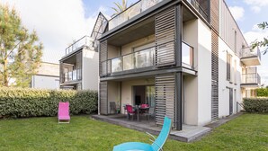 A modern two-story residential building with a balcony, a patio area with outdoor furniture, and a well-maintained lawn. - LE GARDEN - Vaste appartement avec Jardin et terrasse (Dinard)