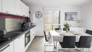 A modern kitchen with white cabinets, a black countertop, and a dining area with a table set for four. - LE GARDEN - Vaste appartement avec Jardin et terrasse (Dinard)