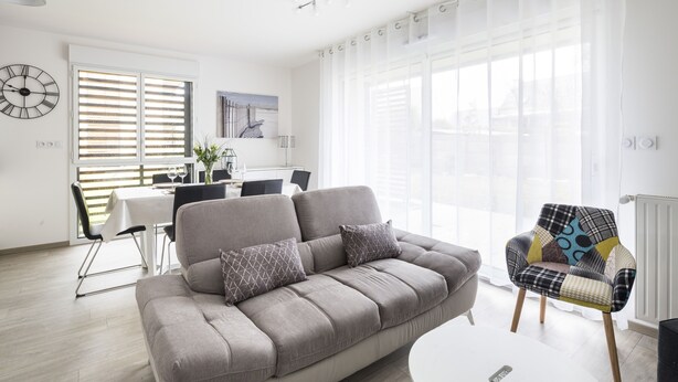 A modern living room with a grey sofa, a patterned armchair, and a dining area with a table and chairs. - LE GARDEN - Vaste appartement avec Jardin et terrasse (Dinard)
