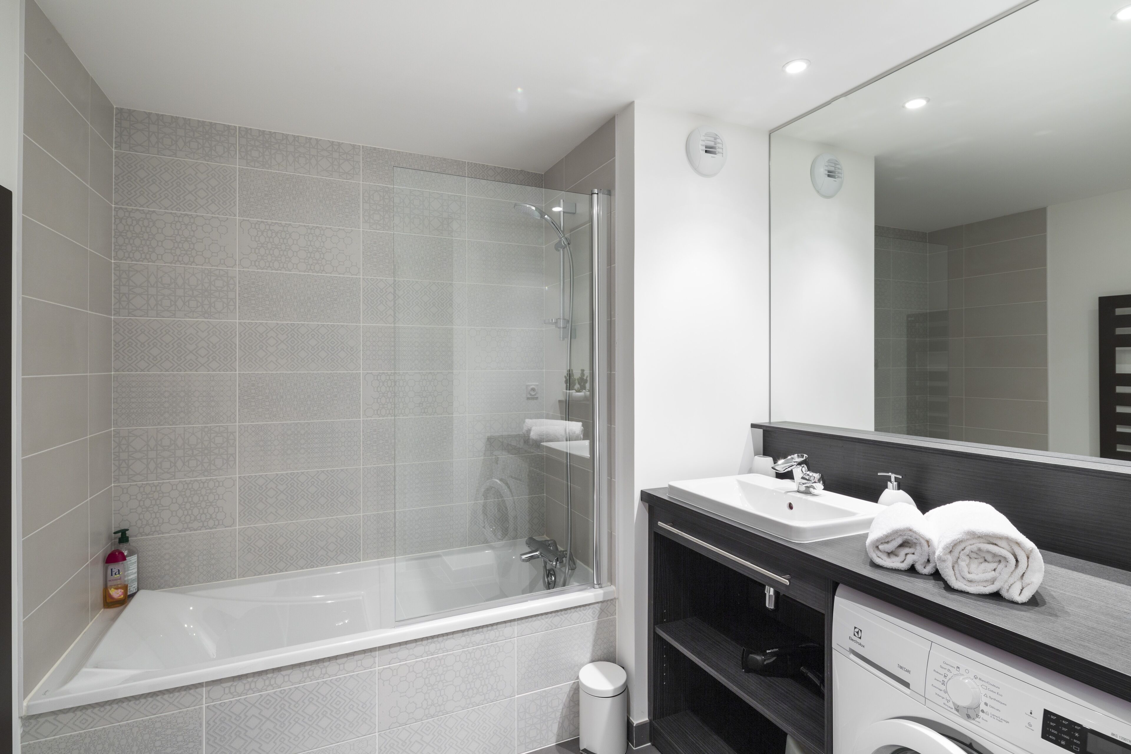 Un baño moderno con ducha envuelta en vidrio, una bañera blanca y un tocador con espejo.