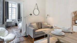 A modern living room with a sofa, a dining table set with plates and glasses, a round mirror on the wall, and a window with curtains. - L'HORLOGE - Cocon de Charme au coeur de Rennes (Rennes)