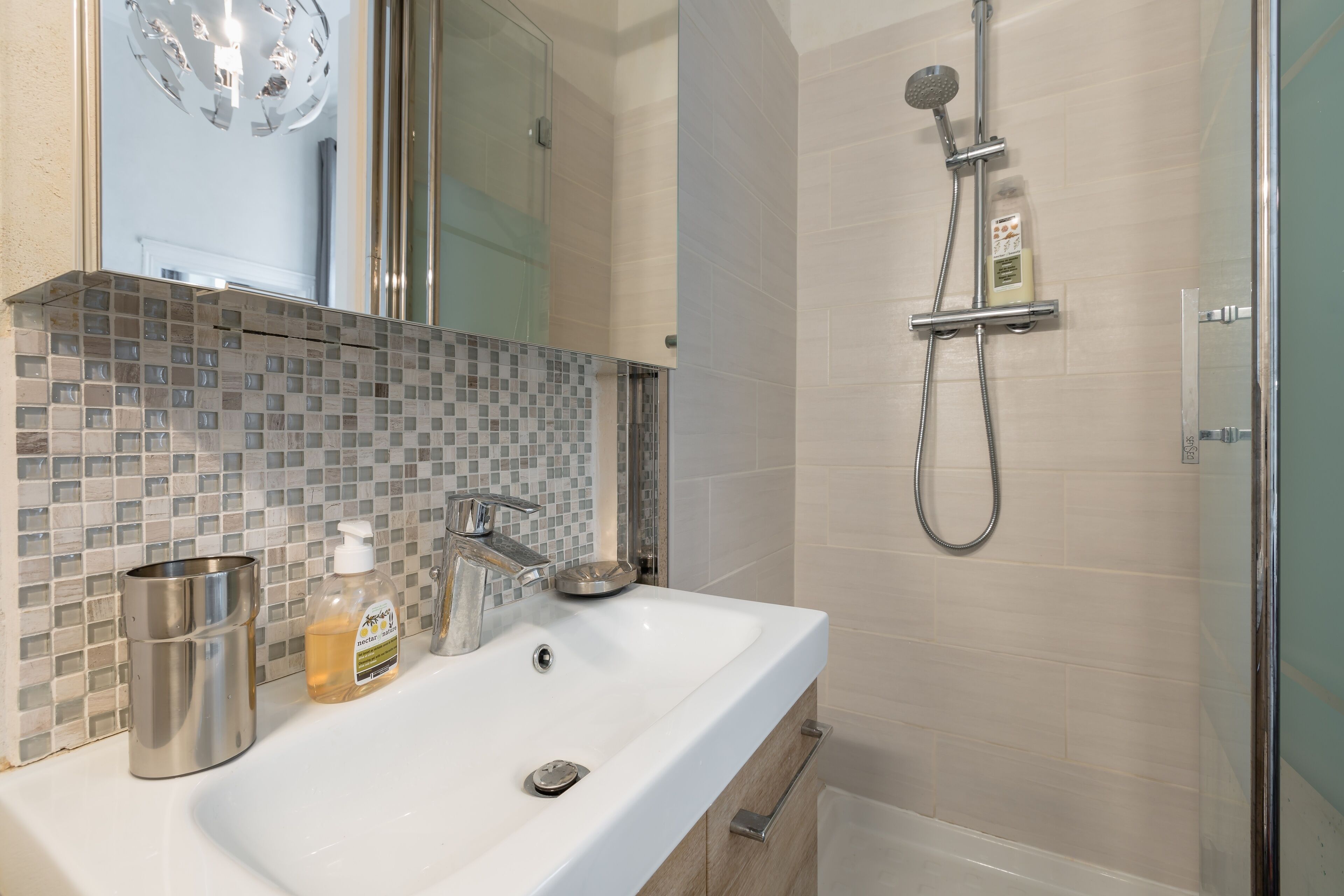 A modern bathroom with a white sink, a glass shower enclosure, and a tiled backsplash.