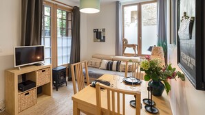 Un salon chaleureux avec un téléviseur, des meubles en bois, une table à manger et une grande fenêtre agrémentée de rideaux.