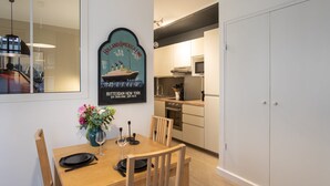 Une cuisine moderne avec un coin repas, comprenant une table en bois dressée pour deux personnes, un vase de fleurs et un tableau encadré représentant un navire.