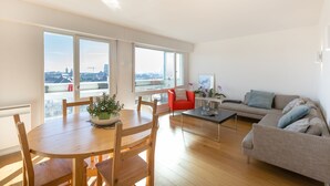 A spacious living room with a dining area, large windows, a grey sofa, and a red chair. - TREGOR - 2 ch - Parking + Vue sublime (Rennes)