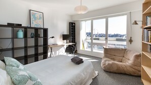 A modern bedroom with a bed, a desk, a chair, a bean bag, and a large window with a city view. - TREGOR - 2 ch - Parking + Vue sublime (Rennes)