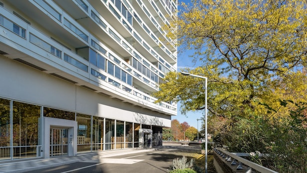 A modern building with a glass facade, a gated entrance, and a tree with yellow leaves in the foreground. - TREGOR - 2 ch - Parking + Vue sublime (Rennes)