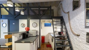 A compact kitchen with a microwave, sink, and a red trash bin. There is a wooden chair and a ladder leading to a loft area. - COCON URBAIN Centre Historique (Rennes)