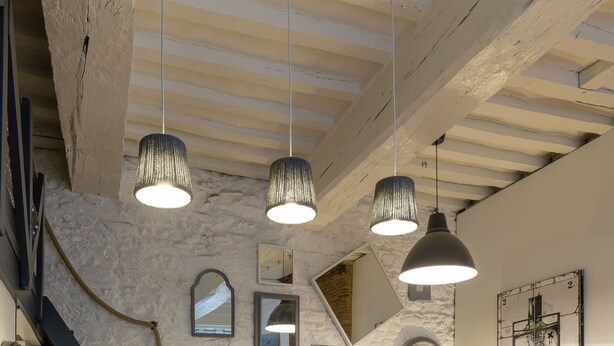 A modern kitchen with a stone wall, wooden ceiling beams, pendant lighting, and a bar area with stools. - COCON URBAIN Centre Historique (Rennes)