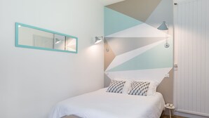A neatly arranged bedroom with a bed, bedside table, and a wall-mounted mirror.