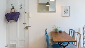 A dining area with a wooden table, blue chairs, a hanging basket, a mirror, and a framed picture on the wall.