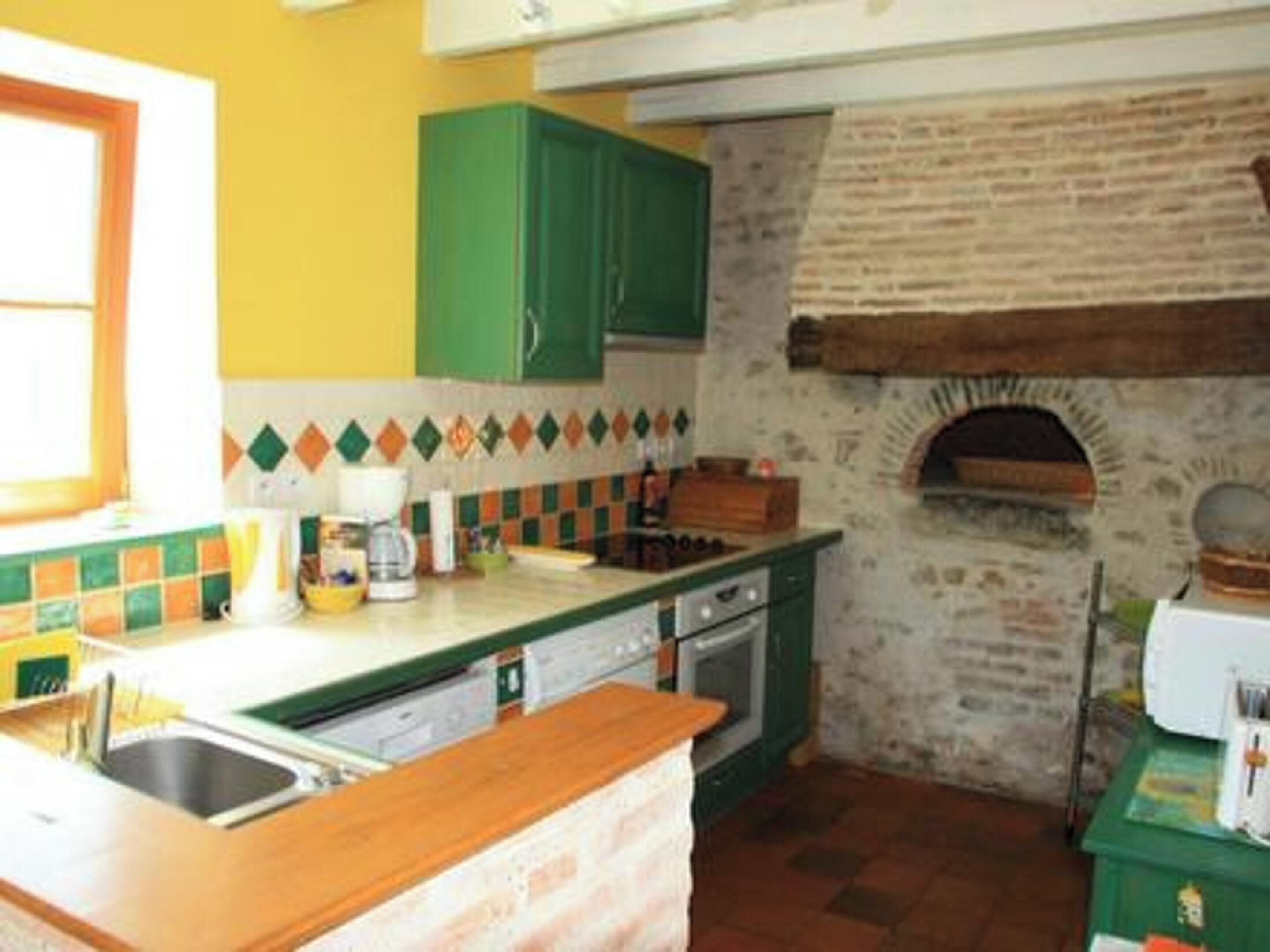 Une cuisine avec un mur recouvert de carreaux, un four en briques, des armoires vertes et une fenêtre.