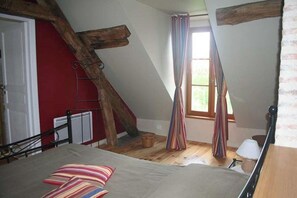 Une chambre avec un plafond en pente, un lit avec des coussins à rayures, une fenêtre avec des rideaux et une échelle en bois.