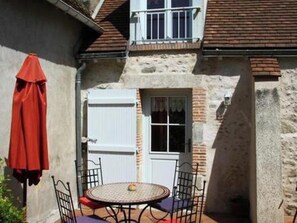 A small patio with a round table and chairs, a red umbrella, and a white door.