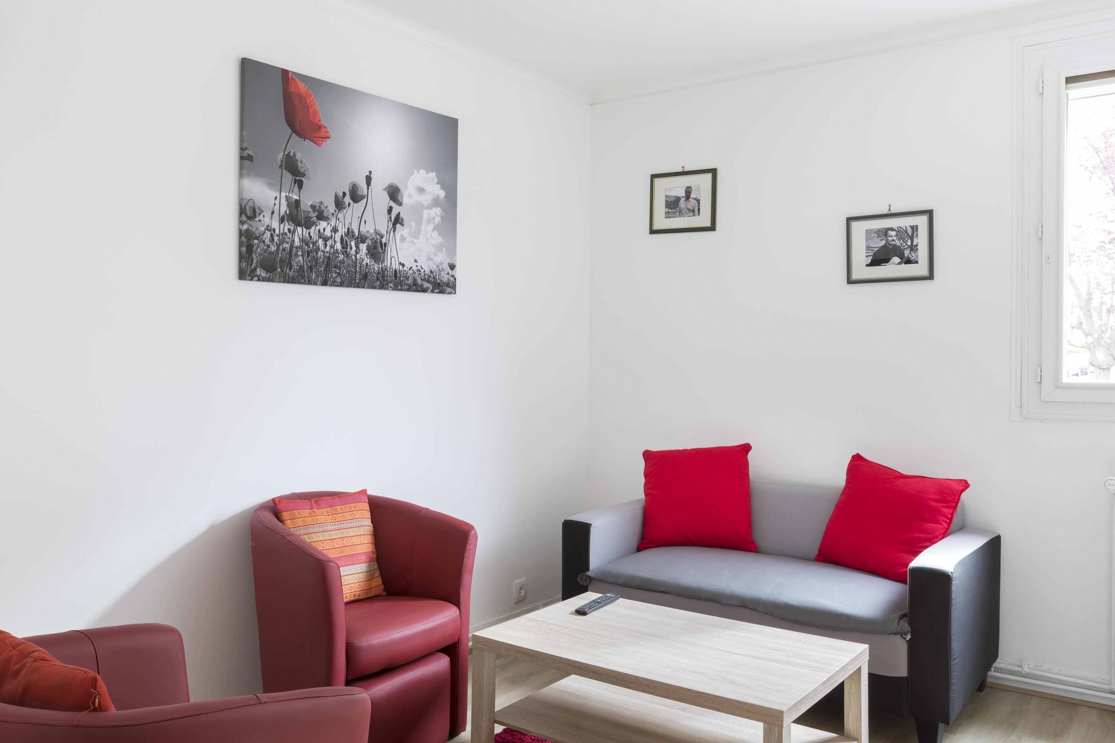 Ein modernes Wohnzimmer mit einem roten Sessel, einem grauen Sofa und einem Couchtisch. An der Wand hängen zwei gerahmte Bilder und über dem Sofa ein großes Gemälde.