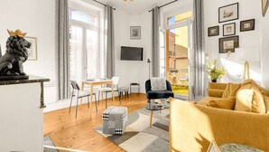 Una sala de estar moderna con un sofá, una mesa de comedor y un televisor. Hay cortinas, una estatua y cuadros en la pared.