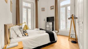 Una habitación de hotel con cama, televisor, piso de madera y ventanas amplias.