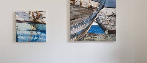 A dark leather sofa with blue and white cushions, a wooden coffee table, and two maritime-themed paintings on the wall.