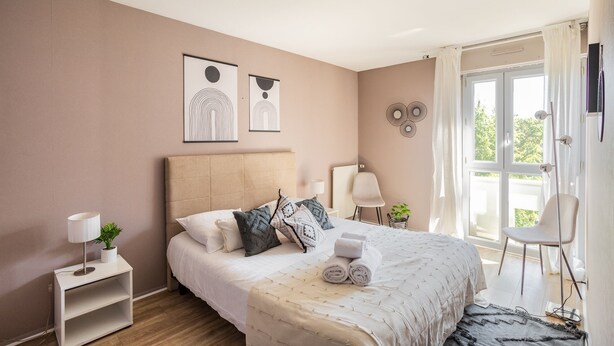 Une chambre à coucher avec un lit, des tables de chevet, une fenêtre avec des rideaux et des œuvres d’art murales.