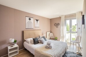Une chambre à coucher avec un lit, des tables de chevet, une fenêtre avec des rideaux et des œuvres d’art murales.
