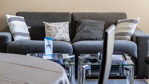 Un salon avec un canapé gris, deux tables d’appoint et des œuvres d’art encadrées accrochées au mur.