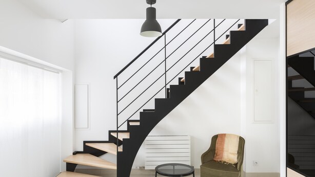 Ein modernes Interieur mit einer schwarzen Treppe, einem runden Tisch und einem grünen Sessel.