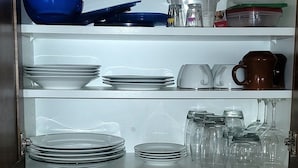 Une cuisine équipée d’un meuble intégré contenant de la vaisselle, des verres et une machine à café. On y trouve également un évier avec un égouttoir et des serviettes pliées.