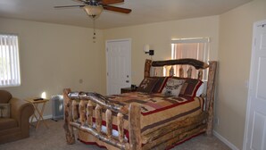 Une chambre avec un lit en bois, un ventilateur de plafond, un radiateur et une fenêtre avec des stores.