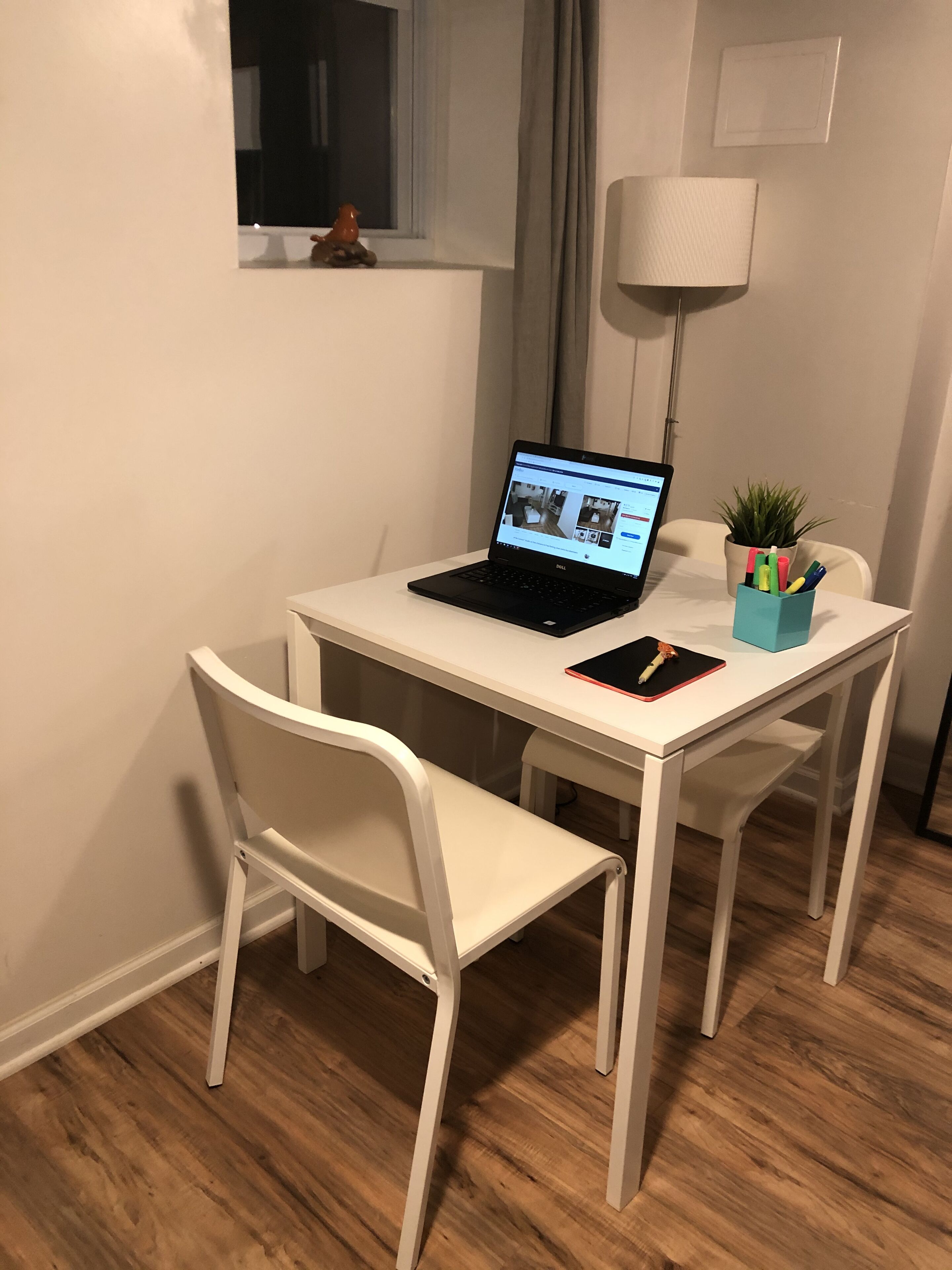 A small, white desk with a laptop, a smartphone, and a plant in a container.