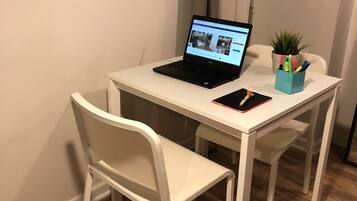 A small, white desk with a laptop, a smartphone, and a plant in a container.