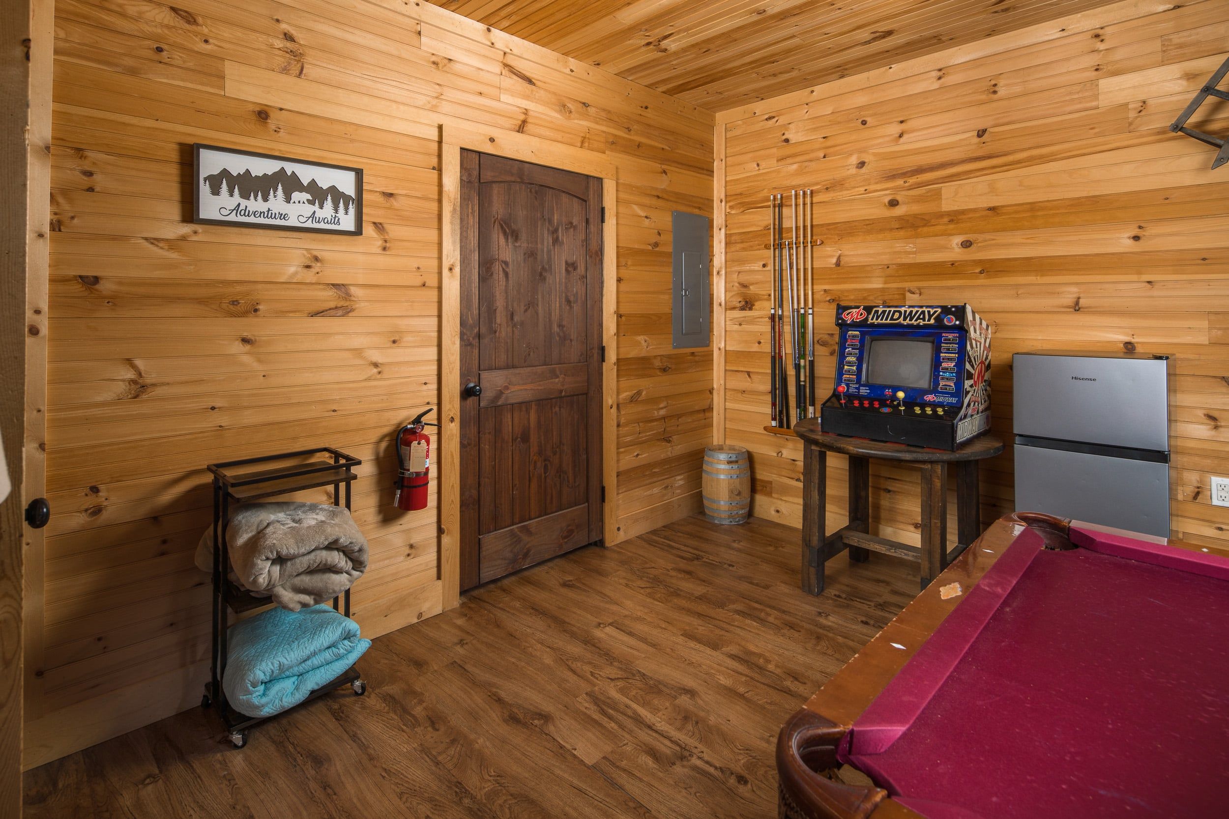 L’intérieur d’un chalet en bois comprend une table de billard, un flipper de la marque Midway, un réfrigérateur et un extincteur.
